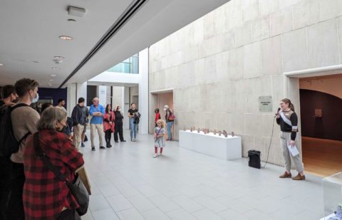 Tour guide with a mic in their hand speaking to an audience at the entrance of the gallery